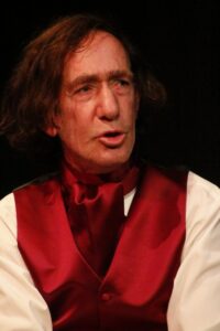 Close-up of Chopin's face in low stage light, lips parted