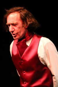 Chopin speaking with his head turned, against a dark stage