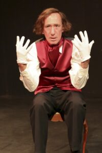 Chopin seated with both white-gloved hands raised, palms forward