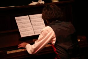 Chopin bent over the piano keyboard, seen from behind, sheet music on the stand