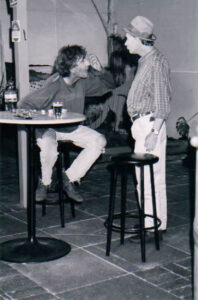 Two men drinking at a table in a country pub, one perched on a bar stool