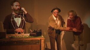 Three actors on stage in The Exchange, one taking a call on a desk telephone