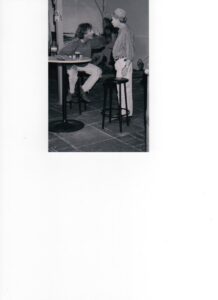 Photograph of two men at a pub table, one seated on a bar stool