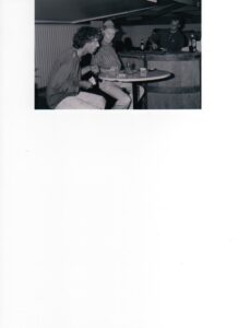 Photograph of two men talking at a pub table with the barman behind them