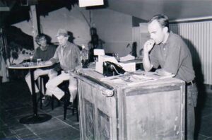 Three men in a country pub interior, one standing at the counter
